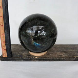 Labradorite sphere on a wooden stand with a ruler for scale against a white background