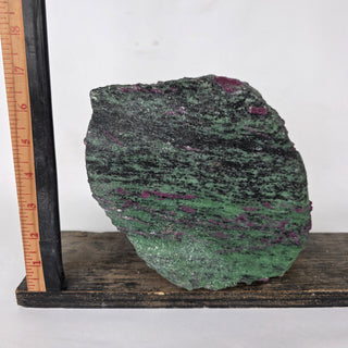 Green mineral sample on a wooden stand with a ruler for scale against a white background