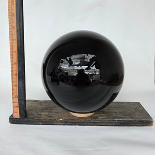 Obsidian sphere on a wooden stand with a ruler for scale against a white background