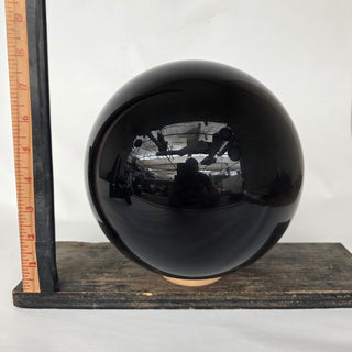 Obsidian sphere on a wooden stand with a ruler for scale against a white background