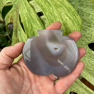 hand holding agate stone pumpkin shape against green leafy background