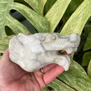 Hand holding a jasper wolf sculpture against a background of large green leaves