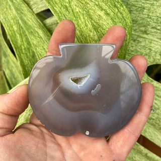 hand holding agate stone pumpkin shape against green leafy background