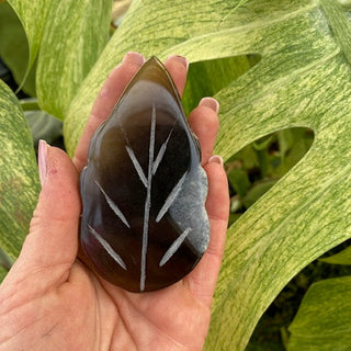 Hand holding a front view of an agate leaf shape carving against green leafy plants