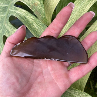 Hand holding agate cloud/mountain shape against a green leafy background