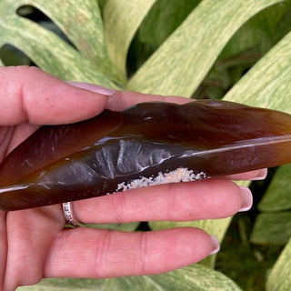 Hand holding agate cloud/mountain shape against a green leafy background