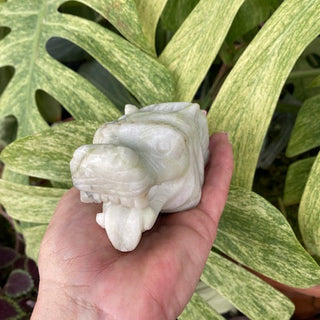 Hand holding a jasper wolf sculpture against a background of large green leaves
