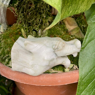 A jasper wolf sculpture sitting on moss of a potted plant